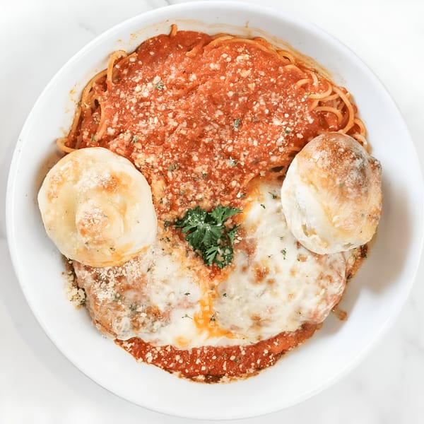 Chicken Parmesan with spaghetti, marinara sauce, melted cheese, and two bread rolls in a white bowl.