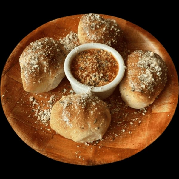 Four golden-brown garlic knots dusted with Parmesan cheese, surrounding a white ramekin of marinara sauce.