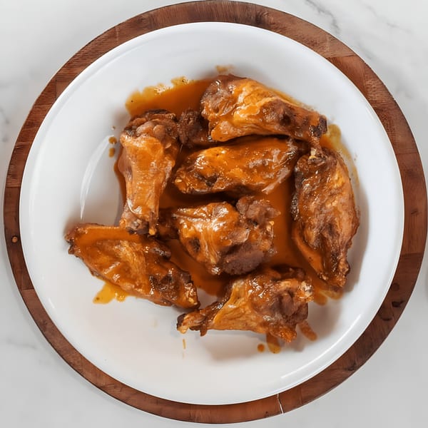 A white plate filled with golden-brown chicken wings drenched in a rich, orange-colored sauce.