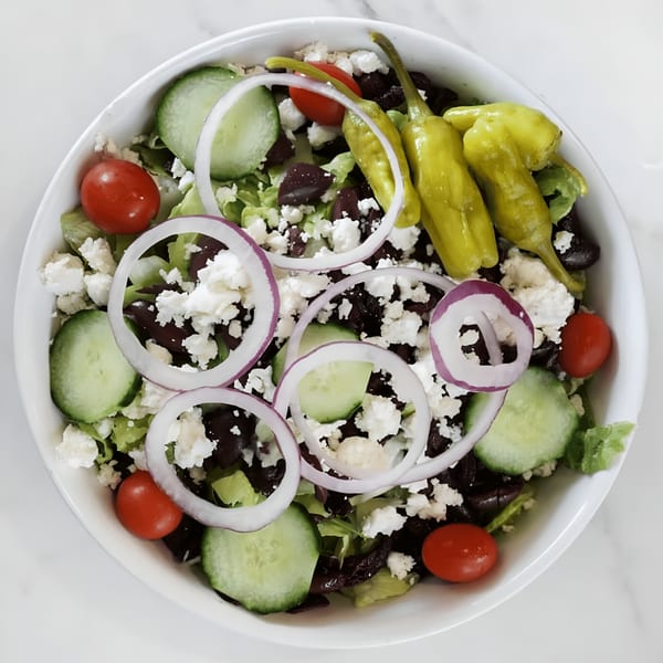 A vibrant Greek salad from Oceanside Pizza, featuring lettuce, cucumbers, tomatoes, olives, feta, onions, and peppers.