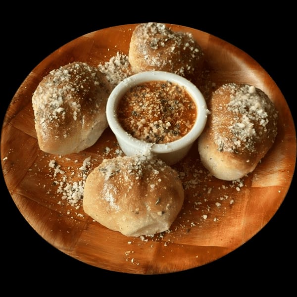 Four garlic knots dusted with Parmesan cheese surround a small bowl of marinara sauce on a wooden plate.