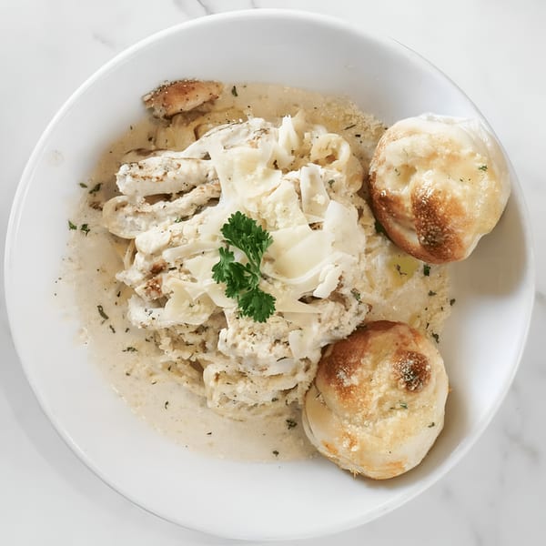 Creamy pasta with shaved cheese and parsley, served with two golden-brown bread rolls in a white bowl.