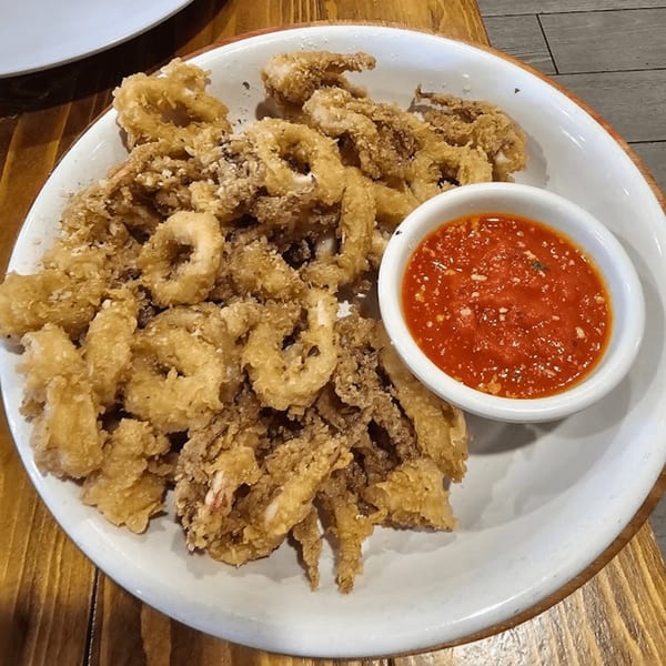 A white plate filled with golden-brown fried calamari rings and tentacles, with a side of red marinara sauce.